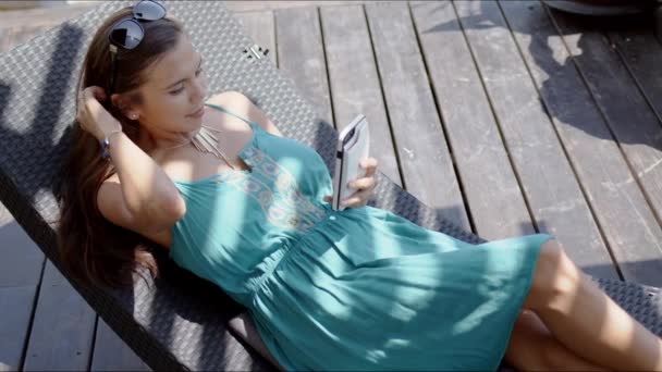 Vrouw in blauwe jurk rustend in lounge stoel en met behulp van smartphone - Video