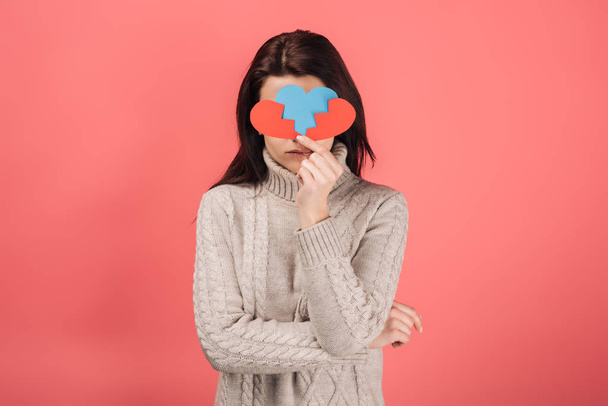 woman covering face while holding blue and red paper cut with broken heart on pink  - Valokuva, kuva