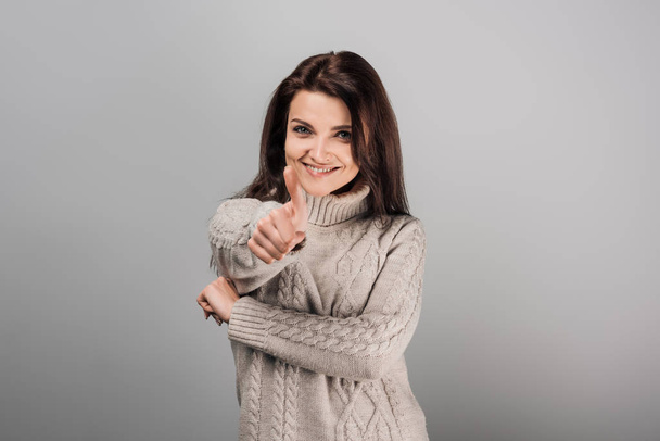 Fröhliche Frau im Pullover zeigt Daumen hoch vereinzelt auf grau  - Foto, Bild