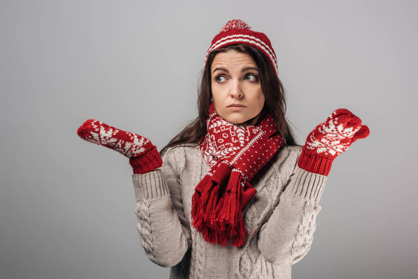 overstuur vrouw in rood gebreide had, handschoenen en sjaal tonen schouders gebaar geïsoleerd op grijs  - Foto, afbeelding