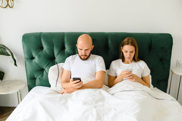 young couple lie in bed with phones. Communication and relationship problems. - Φωτογραφία, εικόνα