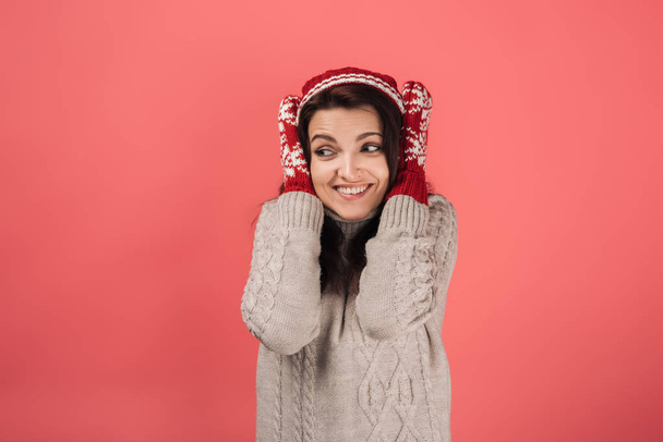 happy woman in knitted hat and gloves covering ears on pink  - Фото, изображение