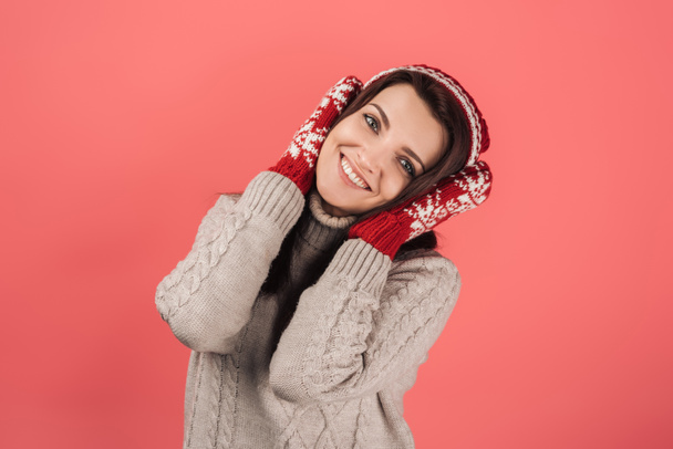 pozitivní žena v pleteném klobouku a rukavicích zakrývající uši izolované na růžové  - Fotografie, Obrázek
