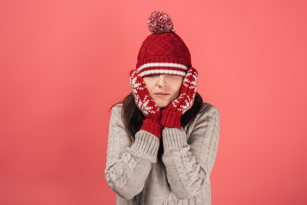 woman in red gloves touching face and covering eyes with knitted hat on pink  - 写真・画像