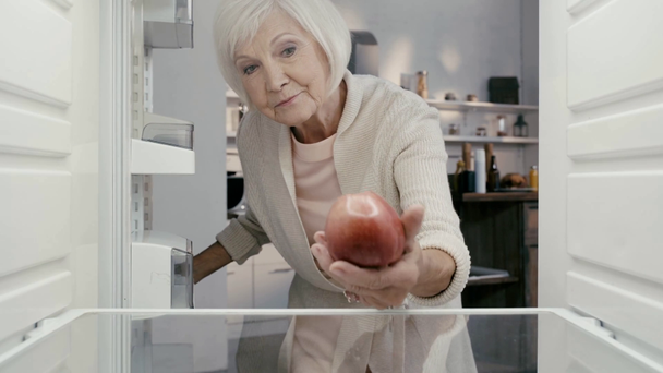 Traurige Frau öffnet Kühlschrank und nimmt Apfel  - Filmmaterial, Video