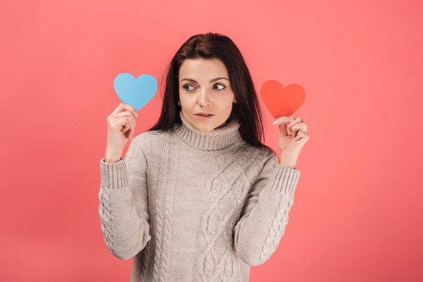 woman in sweater holding blue and red heart-shaped paper artwork on pink  - Photo, image
