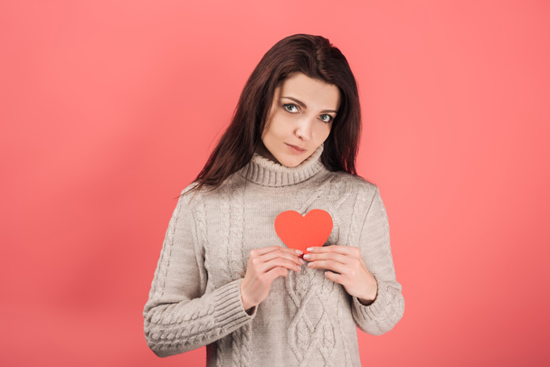 attractive woman in sweater holding heart-shaped paper cut on pink  - Fotografie, Obrázek
