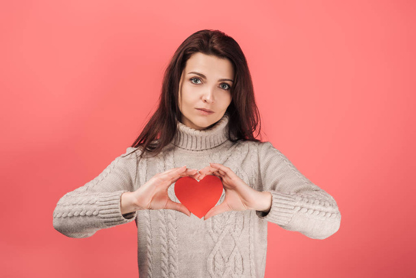 sad woman in sweater holding heart-shaped paper cut on pink  - Photo, Image