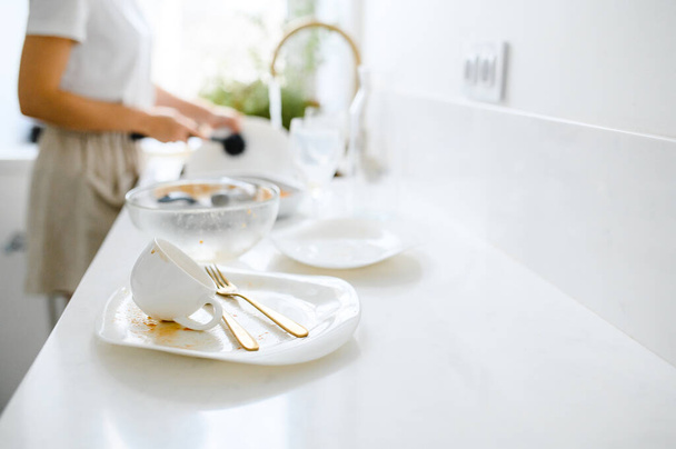 Beautiful smiling young woman washing the dishes in modern white kitchen. - Foto, Imagen