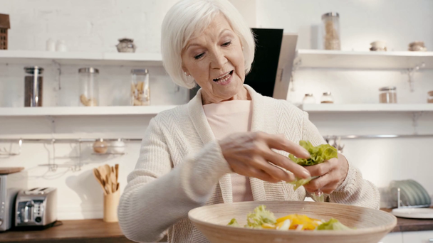 glimlachende vrouw het toevoegen van sla aan salade  - Video