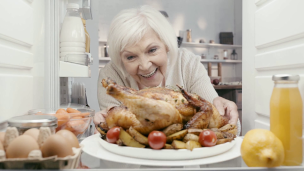 mosolygós nő vesz tányért pulykával a hűtőből - Felvétel, videó