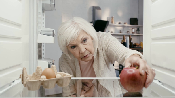 Schockierte Frau öffnet Kühlschrank und nimmt Apfel  - Filmmaterial, Video