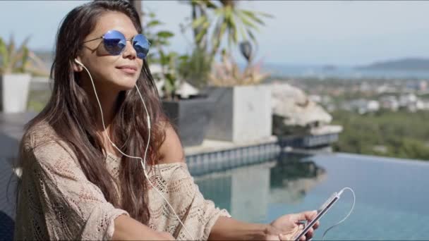 Vrouw luisteren naar muziek aan het zwembad en genieten van zonnige dag - Video