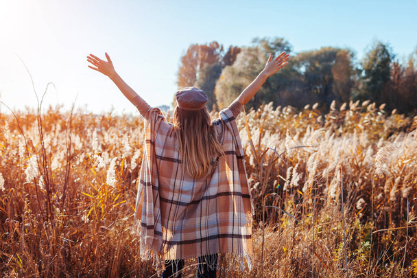 Осенняя мода. Молодая женщина в стильном пончо на открытом воздухе. Одежда и аксессуары. Счастливая девушка поднимает руки
 - Фото, изображение