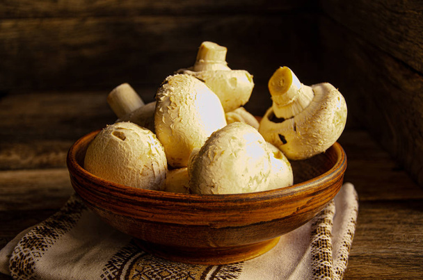 Cogumelos em uma tigela rústica de cerâmica na cozinha em uma mesa de madeira com um guardanapo de cozinha
. - Foto, Imagem