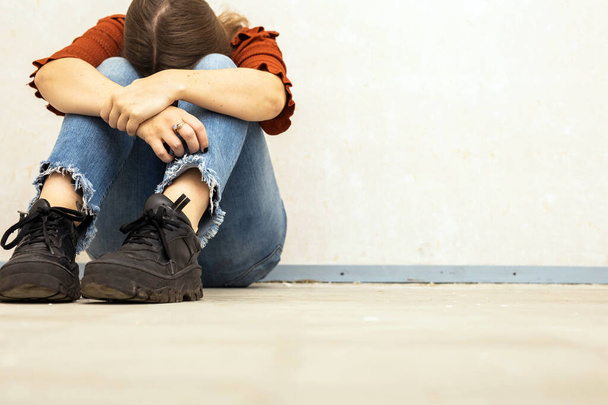 junge Frau weint und sitzt in der Nähe einer leeren Wand, einsames, trauriges und deprimiertes Mädchen mit gesenktem Kopf - Foto, Bild
