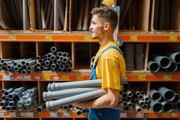 Male builder choosing piping at the shelf in hardware store. Constructor in uniform look at the goods in diy shop - Фото, зображення