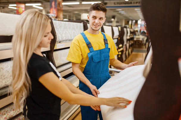 Assistant and female customer choosing wallpapers in hardware store. Seller in uniform and woman in diy shop, shopping in building supermarket - Foto, imagen