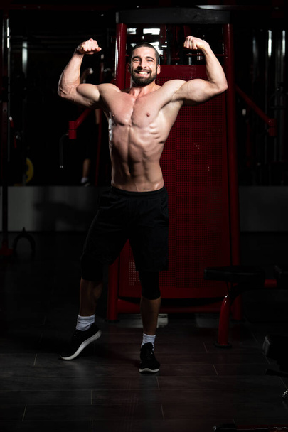 Biceps Pose Of A Young Man In Gym - Foto, afbeelding