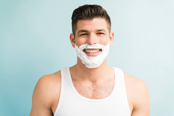 Closeup portrait of smiling attractive Latin male with shaving cream standing against plain background - Foto, Imagen