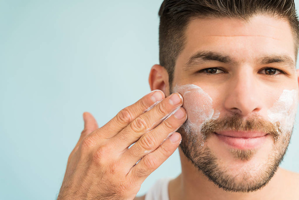 Close-up of attractive male grooming himself with skincare cream on cheeks  in studio - Fotoğraf, Görsel