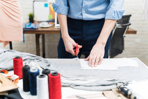 A fiatal szabószövet félbevágása ollóval a munkaasztalon a textiliparban - Fotó, kép