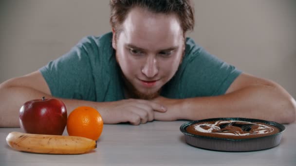 Ο άνθρωπος επιλέγει μεταξύ κέικ και φρούτων στο τραπέζι - Πλάνα, βίντεο