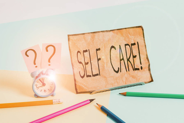 Writing note showing Self Care. Business photo showcasing practice of taking action to preserve or improve ones own health Mini size alarm clock beside stationary on pastel backdrop. - Photo, Image