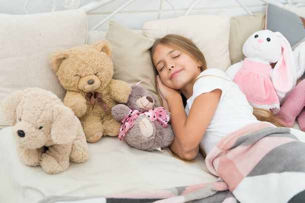 Relaxing before sleep. Girl enjoy evening time with toys. Kid lay bed with toys pillow blanket background. Girl child wear pajamas. Play soft toy before go sleep. Sleep with toy. Carefree childhood - Zdjęcie, obraz