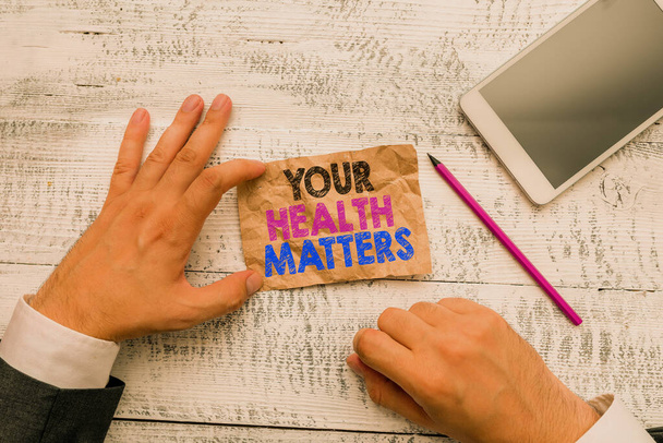 Χειρόγραφο κείμενο Η υγεία σου μετράει. Έννοια που σημαίνει καλή υγεία είναι πιο σημαντικό, μεταξύ άλλων, χέρι κρατήσει σημείωμα χαρτί κοντά στο γράψιμο εξοπλισμού και σύγχρονη συσκευή smartphone. - Φωτογραφία, εικόνα
