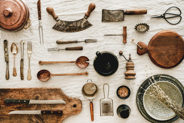 Flat-lay of various kitchen utensils, rustic tablewear, wooden board for cooking, plates, dishes, glasswear, scissors, corkscrew over white linen tablecloth background, top view - Foto, Bild