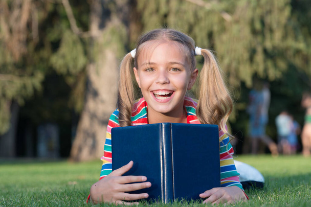 Мое образование пришло из энциклопедии. Счастливая маленькая девочка читает энциклопедию на зеленой траве. Очаровательная детская улыбка с энциклопедией. Энциклопедия и информация
 - Фото, изображение