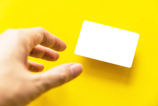 Primo piano mano raggiungendo vuoto biglietto da visita bianco con ombra su sfondo di carta gialla
. - Foto, immagini