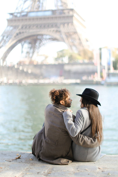 Афро-американец обнимает девушку в шляпе и сидит рядом с Эйфелевой башней, Париж
. - Фото, изображение