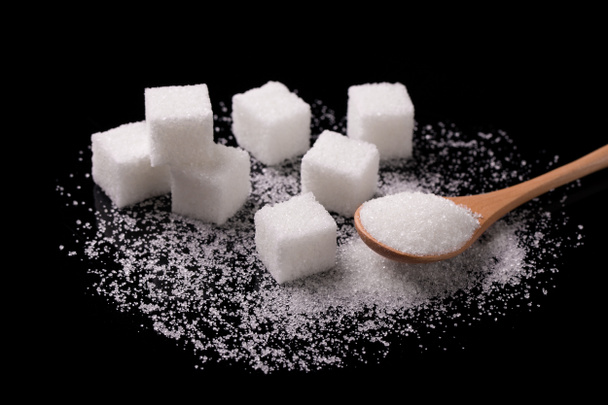 Sugar sand and sugar cubes poured from a wooden spoon. - Photo, Image