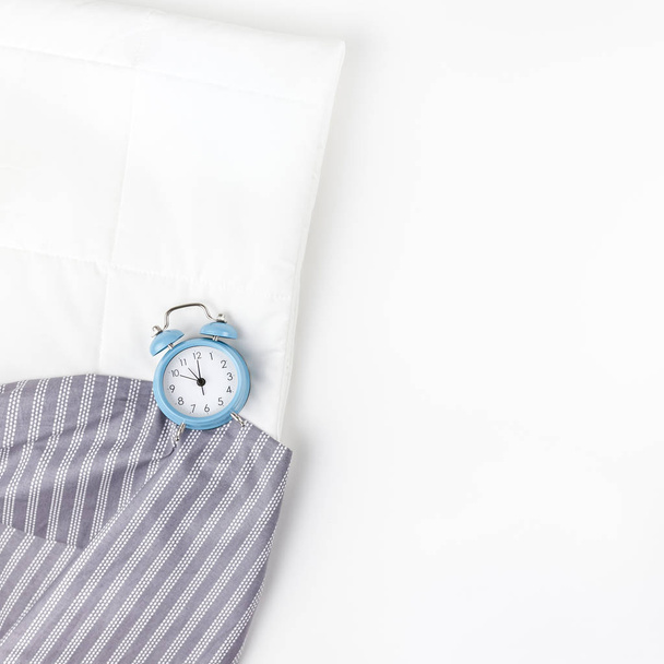 Cama con reloj despertador azul sobre fondo blanco
 - Foto, Imagen