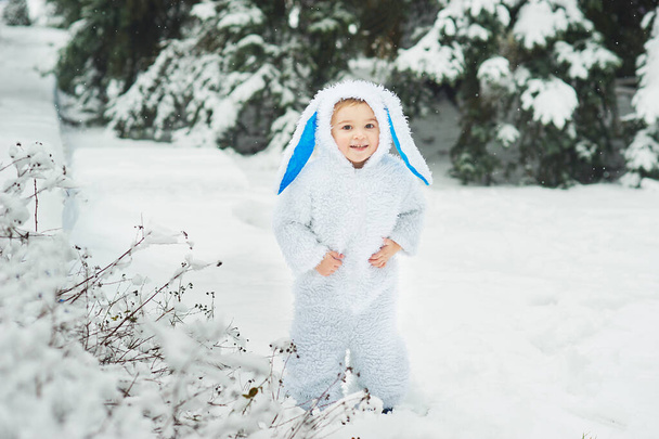 little boy dressed in rabbit costume walking in snowy winter park, christmas and new year  concept   - Фото, зображення