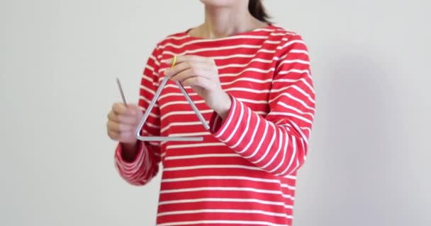 Nierozpoznawalna kobieta w czerwono-białych paskach, grająca na trójkącie. instrument perkusyjny często stosowany w orkiestrach i szkołach muzycznych do edukacji artystycznej - Materiał filmowy, wideo