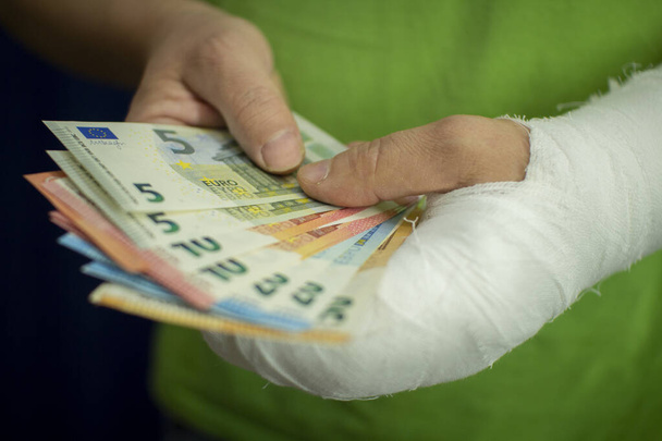 Чоловік з рукою в кастинг тримає гроші від вартості та витрат на екстрену медичну допомогу в лікарні
 . - Фото, зображення