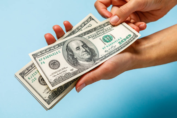 Woman hands counting dollar banknotes on blue background - 写真・画像