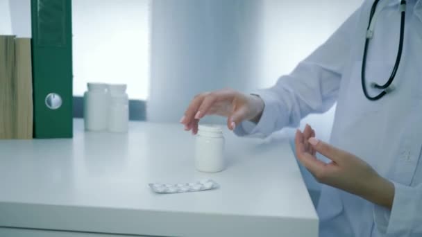 γιατρός χέρια ανοίγει βάζο με συμπληρώματα διατροφής και χύνει κίτρινο στρογγυλό χάπια στην παλάμη σε λευκό τραπέζι - Πλάνα, βίντεο