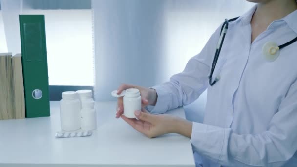 nutritional supplements, doctor dietician hands opens jar of vitamins and pours yellow round pills into palm on white table - Materiał filmowy, wideo