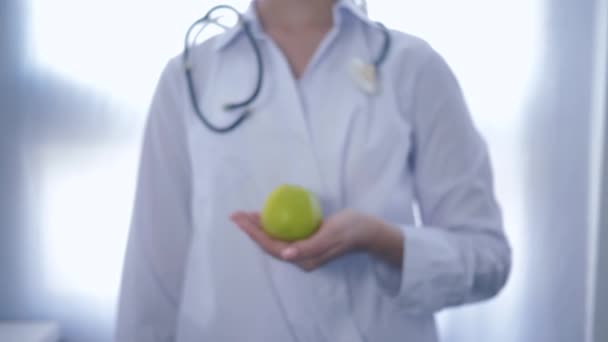 Ernährungswissenschaftlerin mit grünem Apfel in der Hand streckt sich in die Kamera und rät zu gesunder Ernährung für Wohlbefinden, unkonzentriert - Filmmaterial, Video