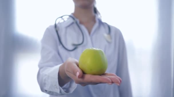 professional expert on food with green apple in hands gives into camera advising healthy diet for wellness, unfocused - Πλάνα, βίντεο