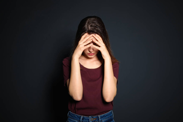 Young woman covering face against dark background - Foto, imagen