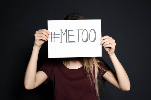 Young woman holding #METOO card against dark background - Foto, Imagem
