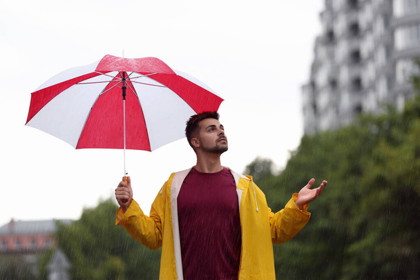 Handsome young man with bright umbrella outdoors on rainy day - Fotografie, Obrázek