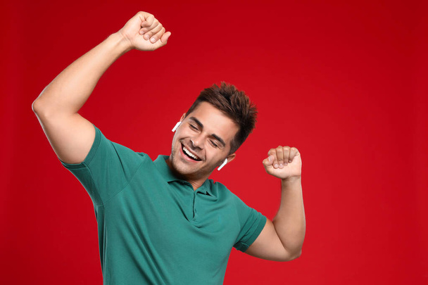 Happy young man listening to music through wireless earphones on red background - Foto, Imagen