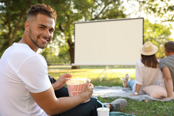Young man with popcorn watching movie in open air cinema. Space for text - Photo, Image