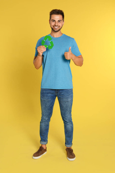 Young man with recycling symbol on yellow background - Photo, image